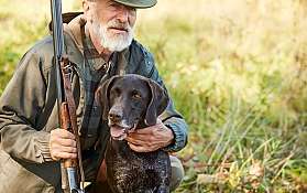 Jäger mit Hund im Freien Ein älterer Mann mit einem Hund und einem Gewehr in der Natur.