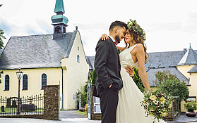 Brautpaar vor Kirche Ein Brautpaar umarmt sich vor einer Kirche im Freien.