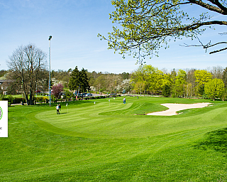 Grüner Golfplatz mit Spielern und Sandbunker im Hintergrund.