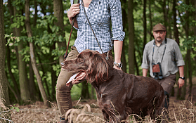 Een oudere man met een hond en een geweer in de natuur.