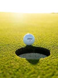 Ein Golfball steht vor einem Golfloch auf grünem Rasen.