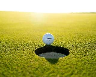 Ein Golfball steht vor einem Golfloch auf grünem Rasen.
